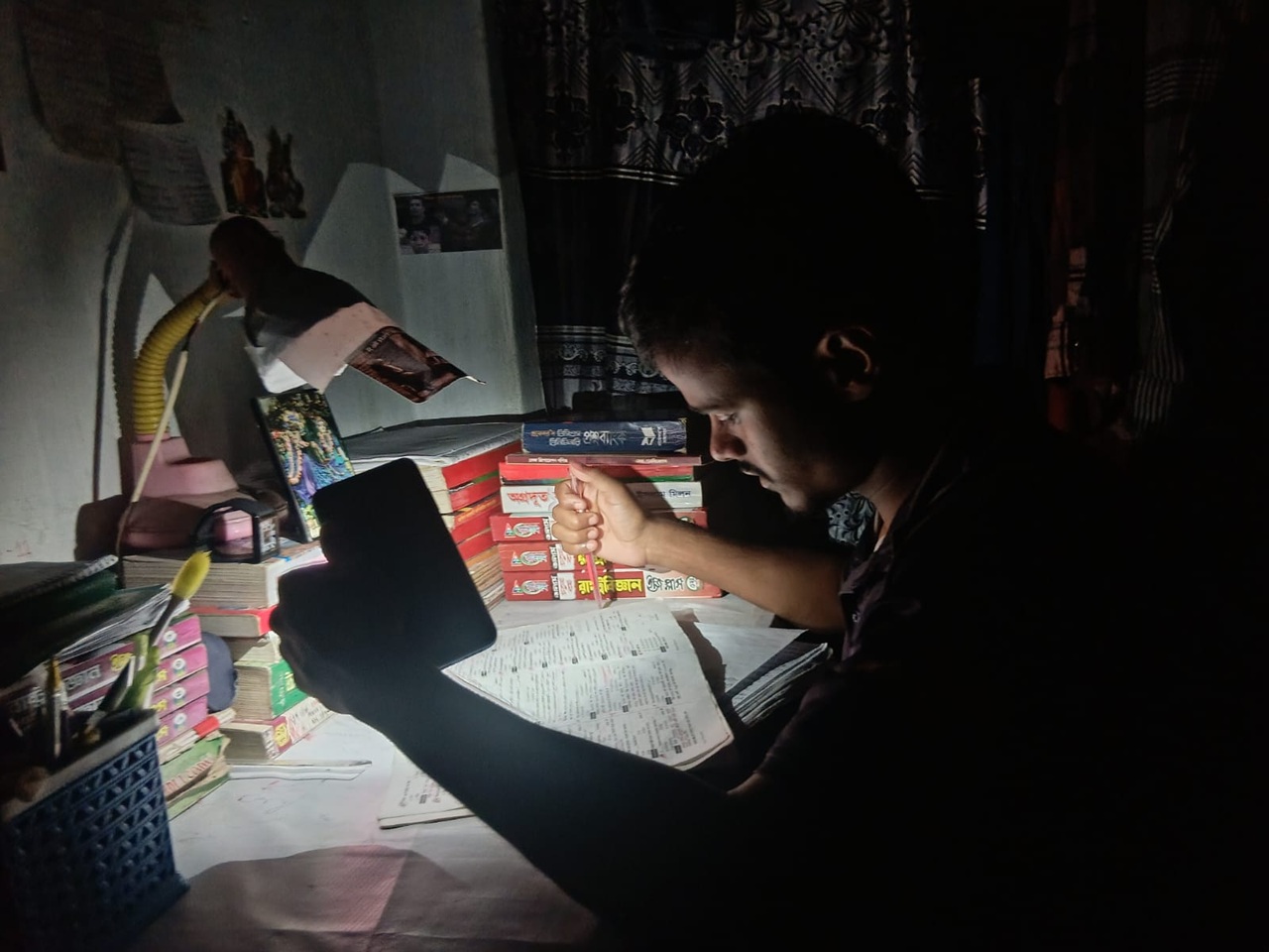 মোবাইল ফোনের টর্চ জ্বালিয়ে পড়াশোনা করছেন এক শিক্ষার্থী। ছবি: চরচা